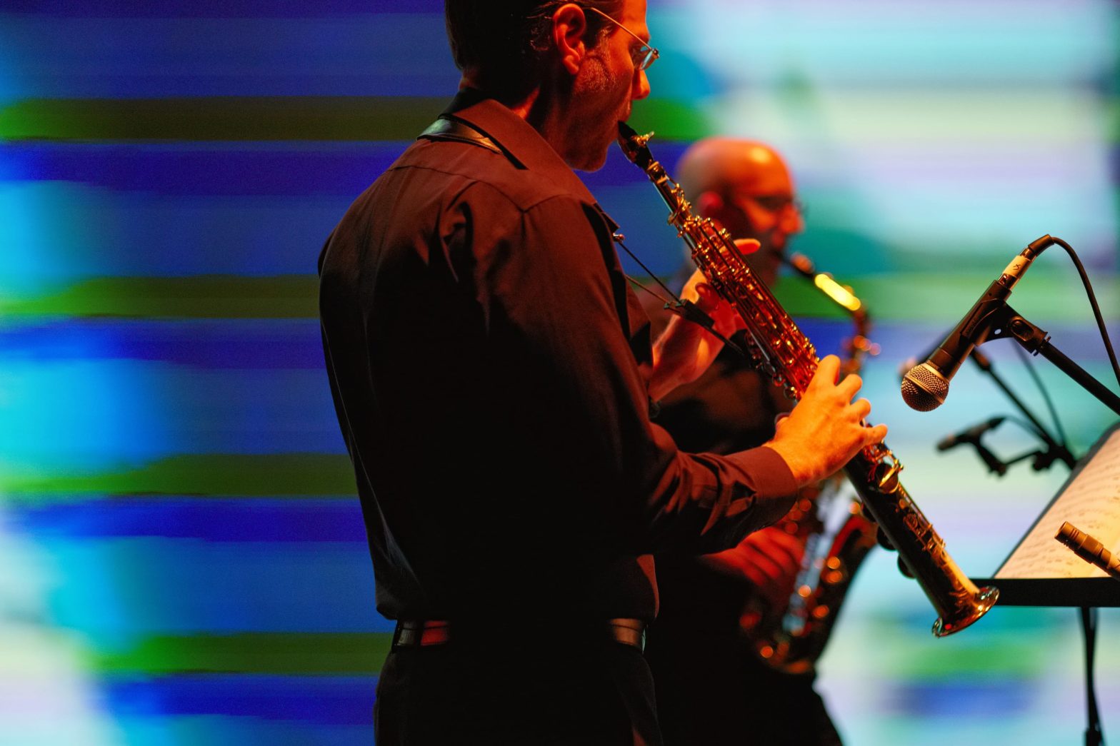 PRISM soprano saxophonist Timothy McAllister and alto saxophonist Zachary Shemon performing in front of a soft-focus blue and green video screen